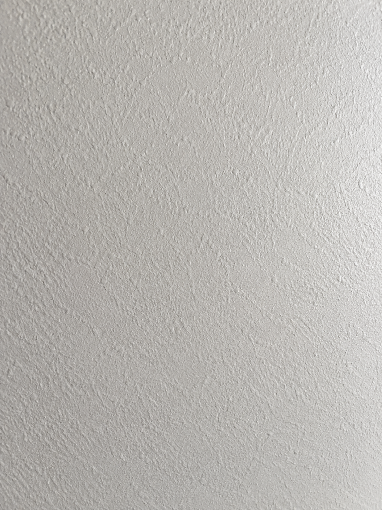 Close-up of a white textured wall with a rough, stippled plaster finish.